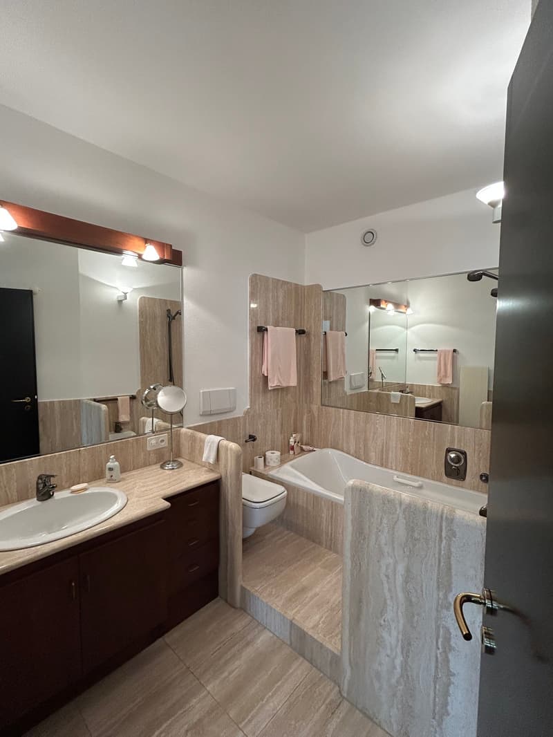 modern bathroom with large mirror, bathtub, sink, toilet, wooden cabinets, marble flooring, pink towels