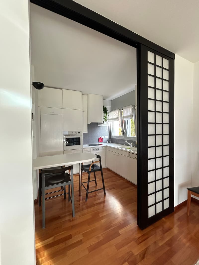 modern kitchen with white cabinets, wooden floor, white table, black chairs, sink, oven, dishwasher, microwave