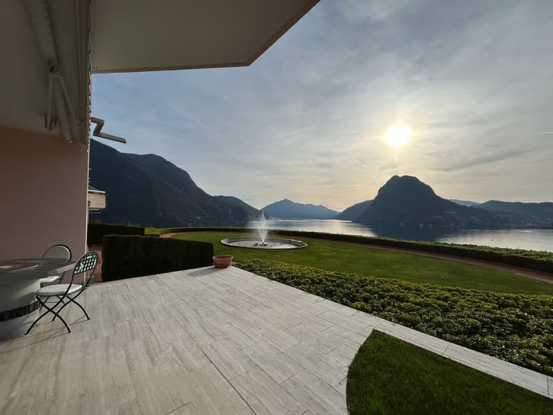 Outdoor terrace with a table and chairs, fountain, and a view of a lake and mountains