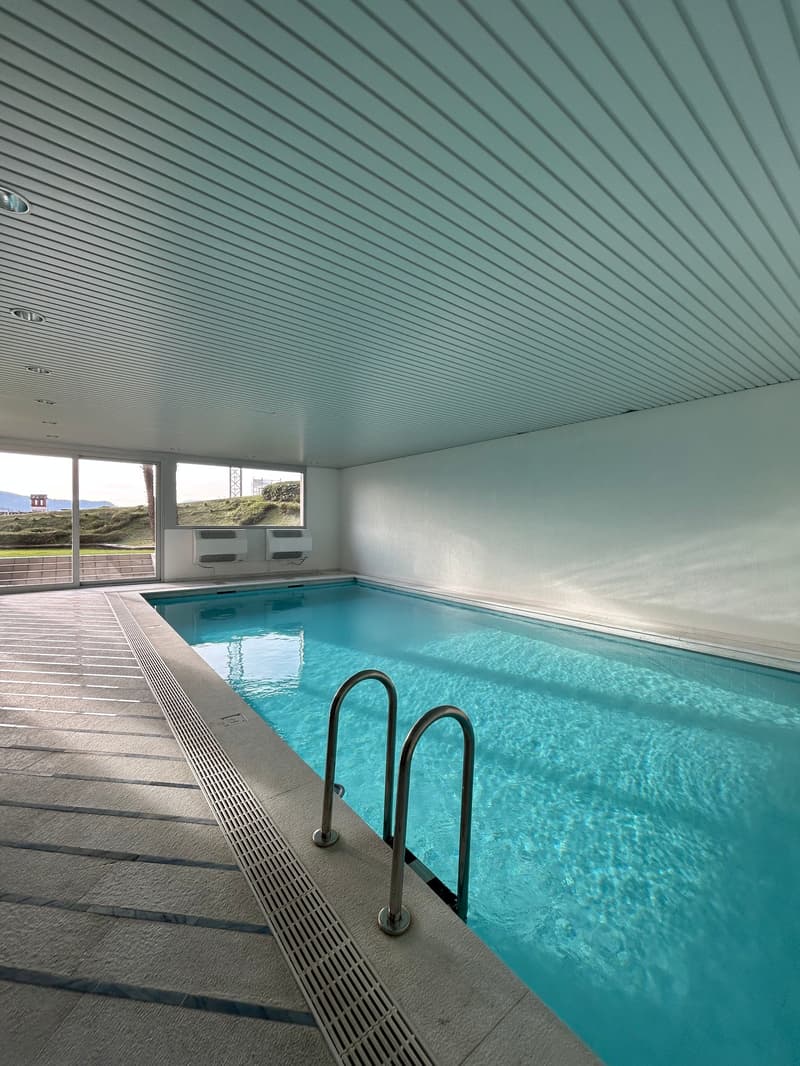 Indoor swimming pool, white walls, glass windows, metal handrails, tiled floor