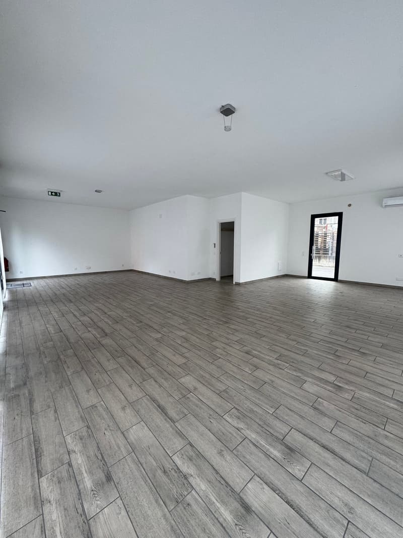 Empty room with wooden floor, white walls, ceiling lights, and an open door leading to another room.
