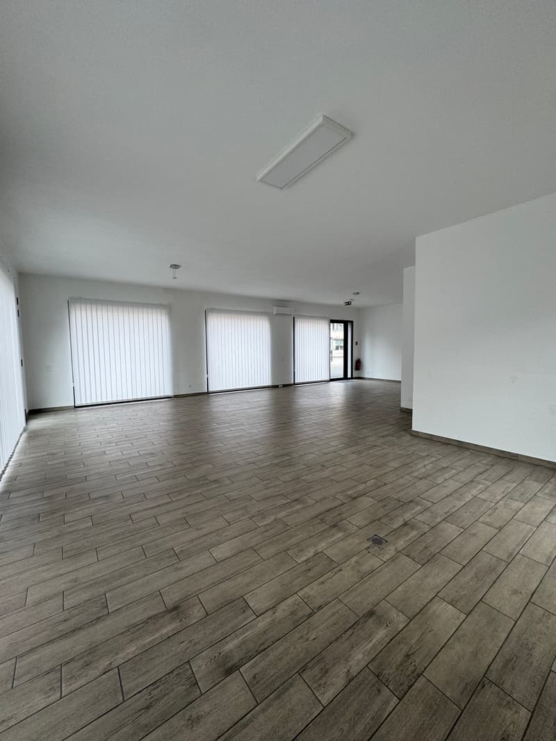 Empty room, wooden floor, white walls, large windows, ceiling lights, air conditioning unit