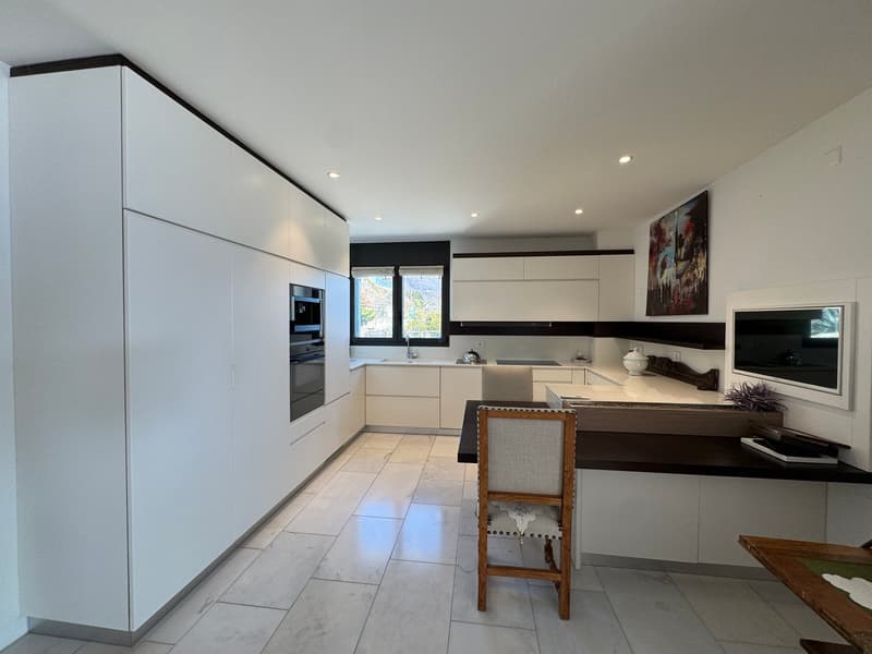 Modern kitchen with white cabinets, tiled floor, wooden chair, kitchen island, gas stove, oven, dishwasher, sink, picture frame, television