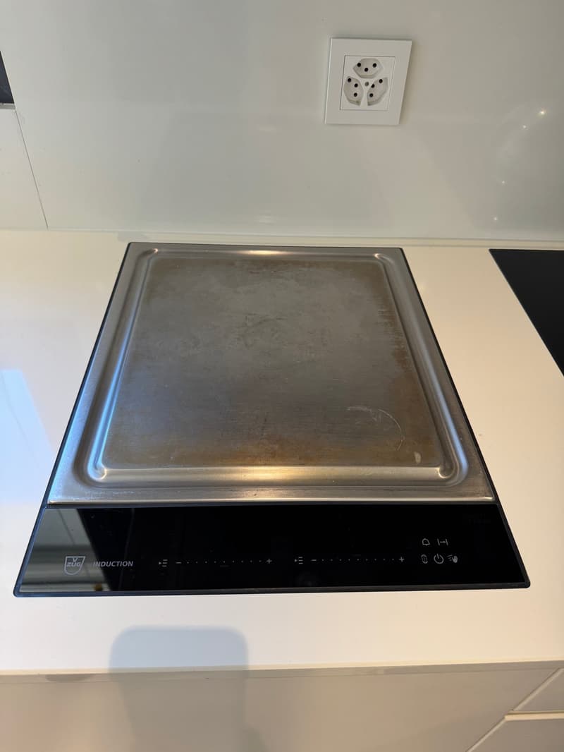 Stainless steel induction cooking surface, black frame, digital controls, power outlet behind