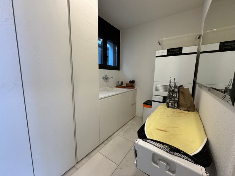 A small room with white cabinets, sink, washing machine, and a window.