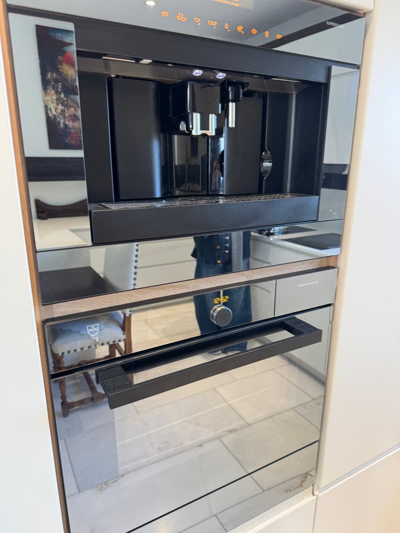 Kitchen with integrated black oven and coffee machine, stainless steel cabinets, tiles
