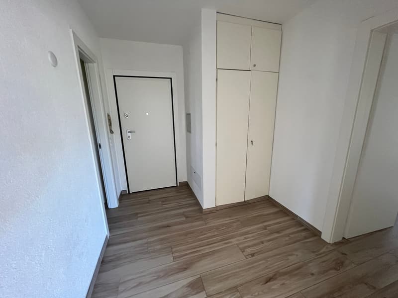 Empty room with wooden floor, white walls, white door, and white cabinets