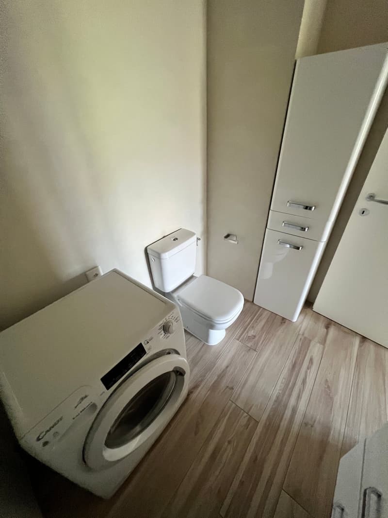 A small bathroom with a toilet, a washing machine, and a cabinet