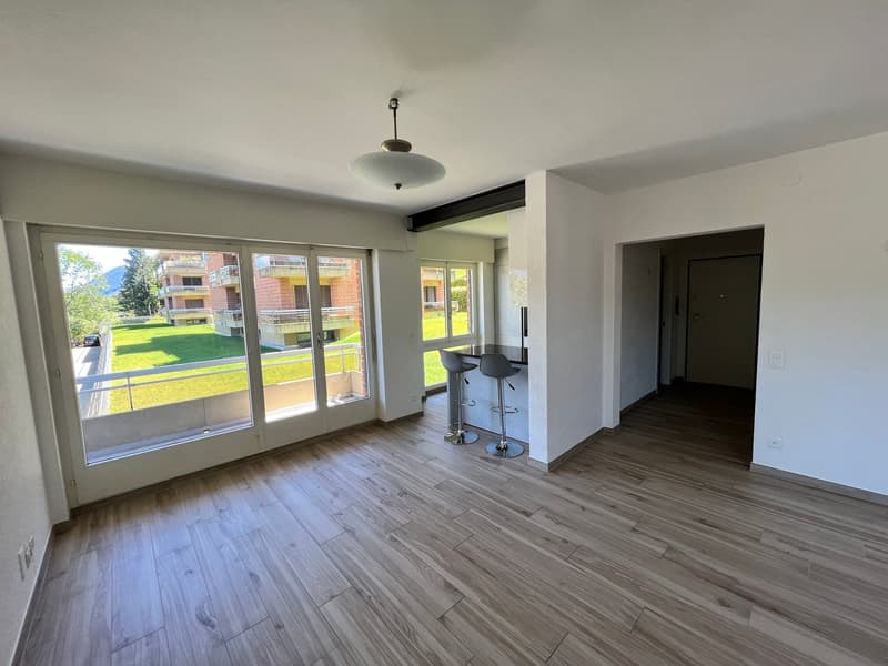 empty room, wooden floor, large windows, balcony, kitchen area with stools