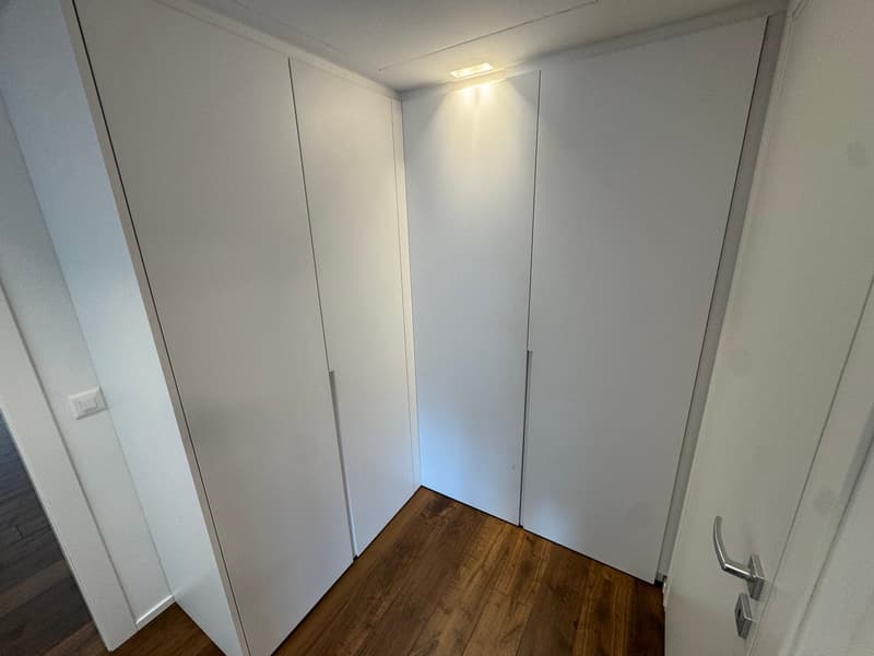 Empty room with white walls, wooden floor, and built-in wardrobes