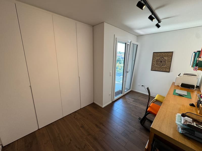 spacious room, wooden floor, large white wardrobe, desk, chair, sliding glass door, picture frame, printer, books, office supplies