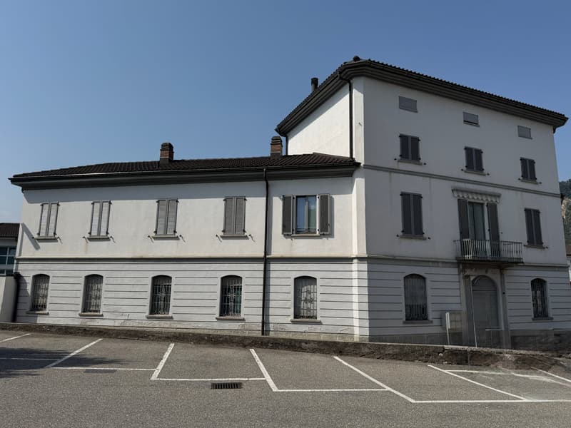 3 story building, white exterior, multiple windows, brown roof, parking lot in front