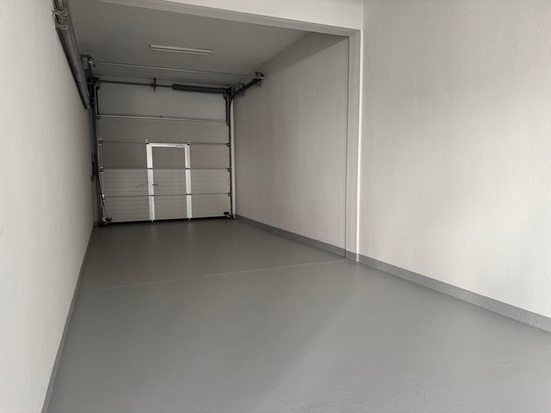 empty concrete floor, white walls, overhead light, garage door