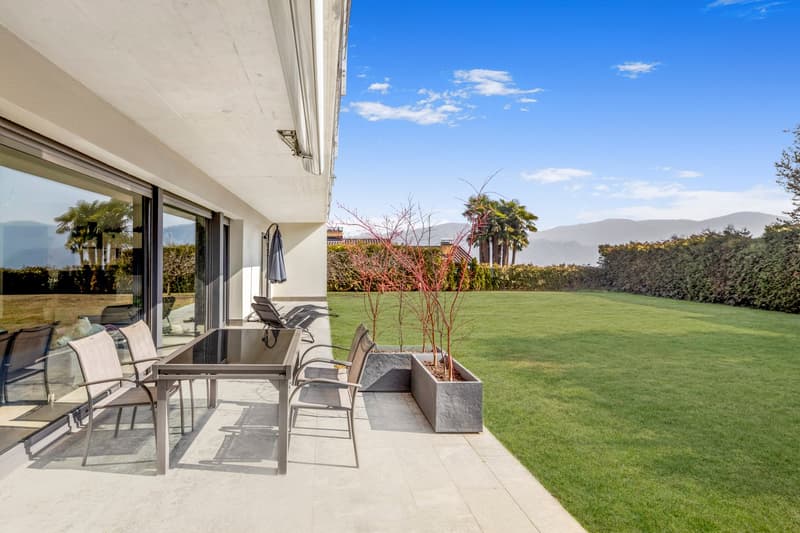Spacious outdoor patio with seating area, large windows, green lawn, palm trees, and scenic mountain view in the background