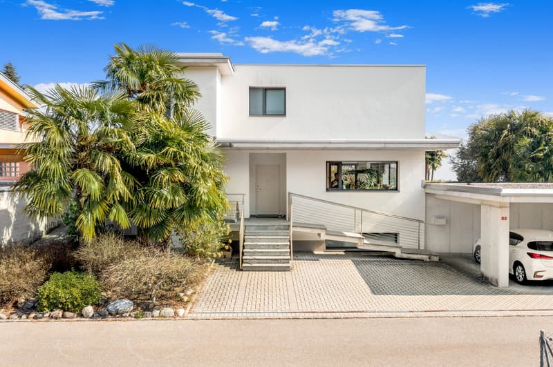 Two-story white modern house with palm trees, paved driveway, and a parking space
