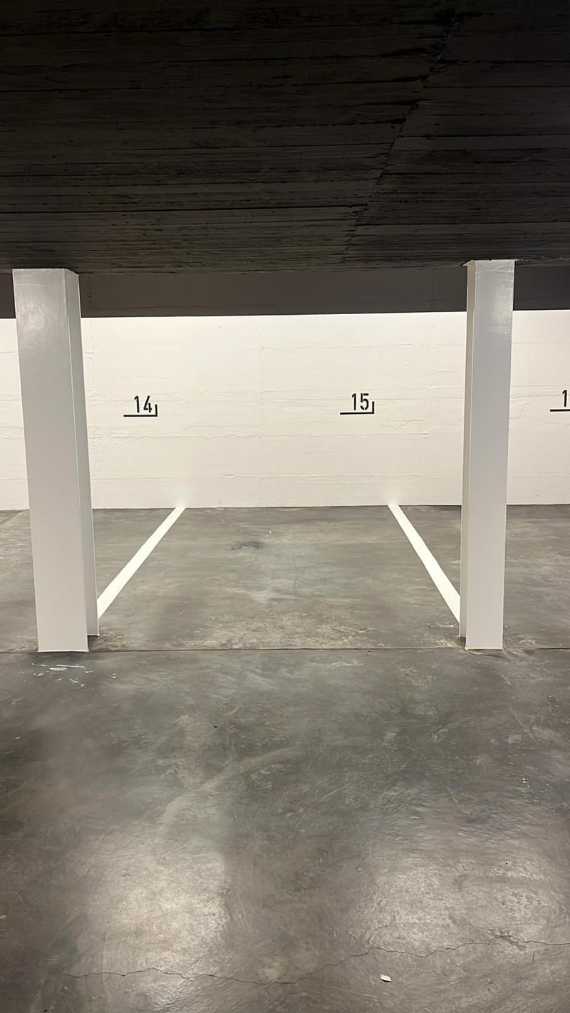Underground parking lot with two parking spaces labeled 14 and 15, white walls, gray concrete floor, white pillars
