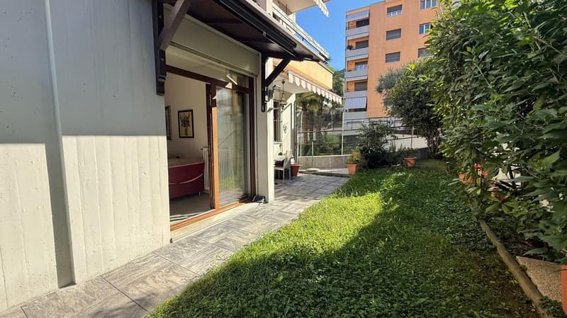 A patio with tiles, surrounded by plants, a potted plant, and a red bed