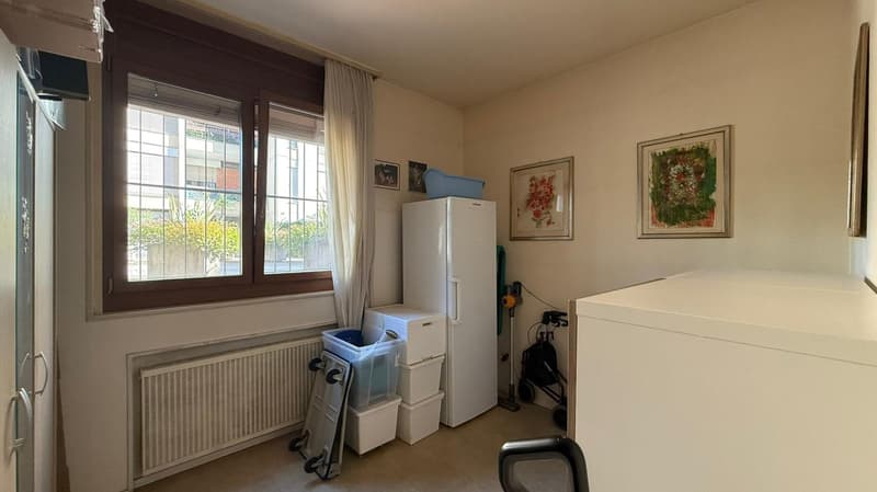 A small room with white appliances and decorations on the wall. A white refrigerator, a washing machine, and plastic storage containers are arranged against the wall. A radiator is also mounted below the window.