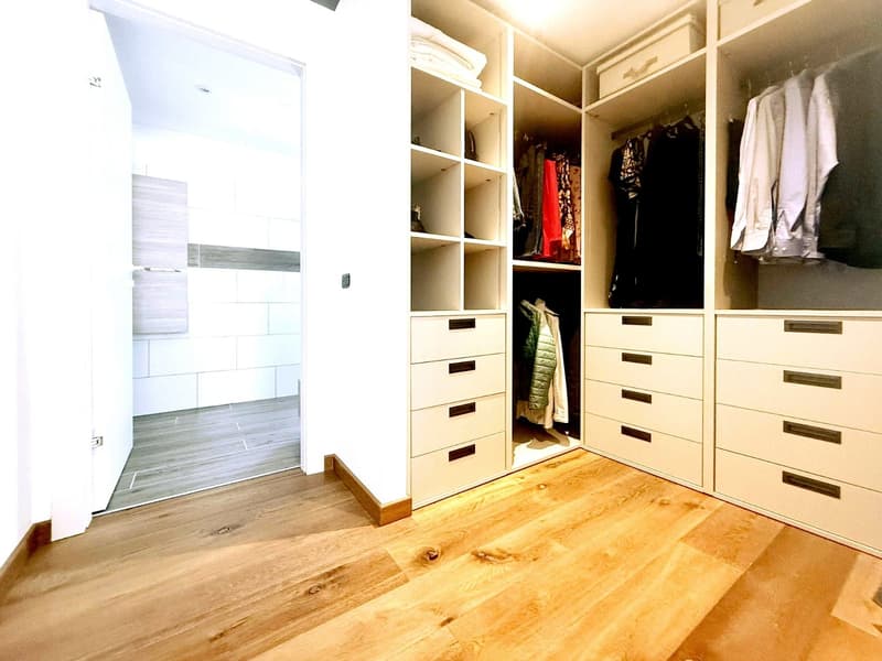 walk-in closet with wooden floor, white walls, built-in wardrobes, drawers, shelves, and hanging space for clothes
