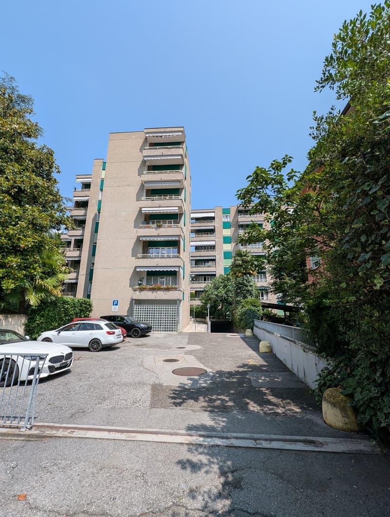 An apartment building with many floors and parking spaces in front of it.