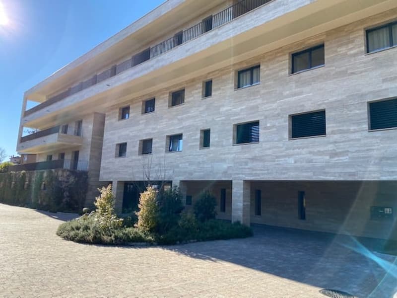 Modern apartment building with stone facade, multiple balconies, and a driveway