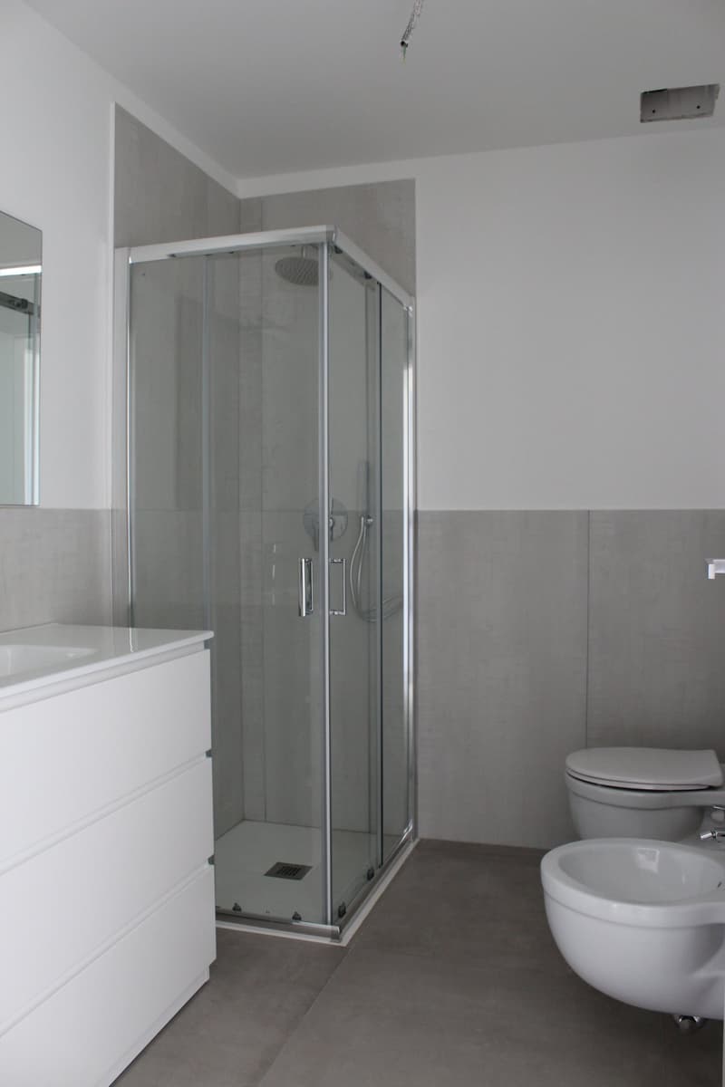 modern bathroom with glass shower, white sink, white toilet, white bidet, white tiles