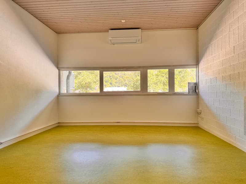 An empty room with yellow flooring, white walls, large windows, and an air conditioning unit mounted on the wall.