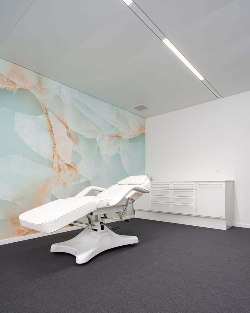 Medical examination room with a white reclining chair and a large white marble-like mural on the wall