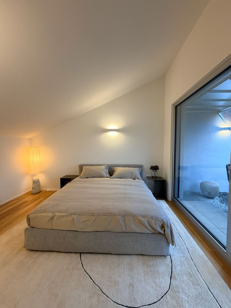 A large bed with two nightstands, a lamp, large window, and a carpet