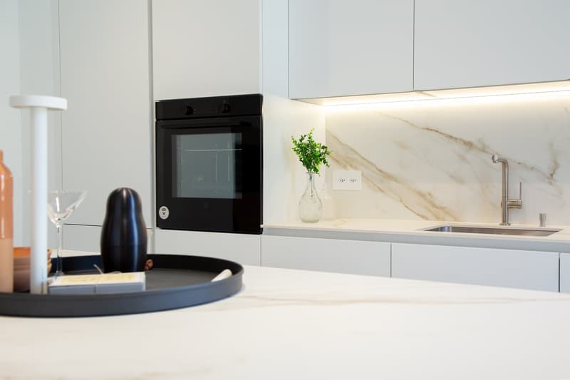 modern kitchen, black oven, white countertops, kitchen island, stainless steel sink, marble backsplash, under-cabinet lighting