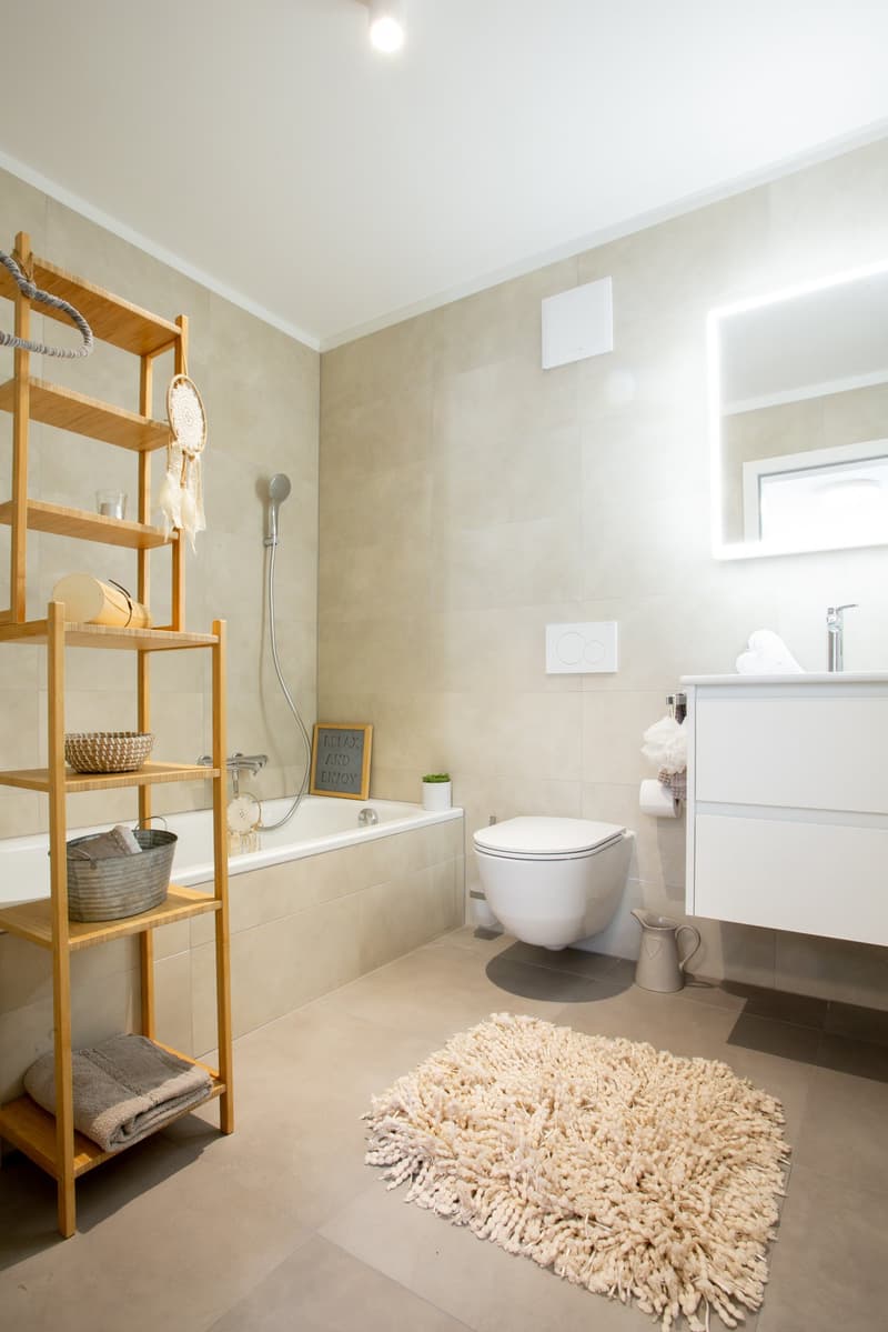 Bathroom: white tile, bathtub, wooden shelf, white toilet, white vanity, mirror, rug