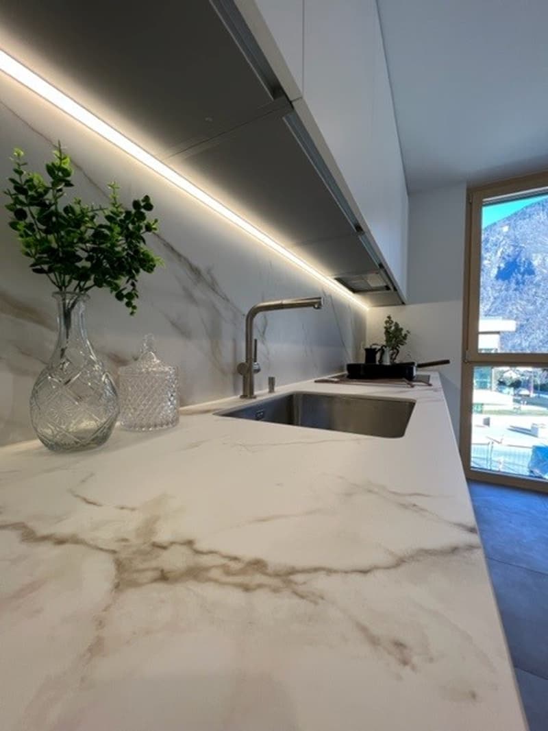 modern kitchen with white marble countertops, glass vase, and potted plant on the counter, stainless steel sink, and faucet
