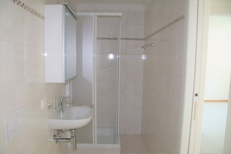 Bathroom with white tiles, sink, shower enclosure, and a power outlet.