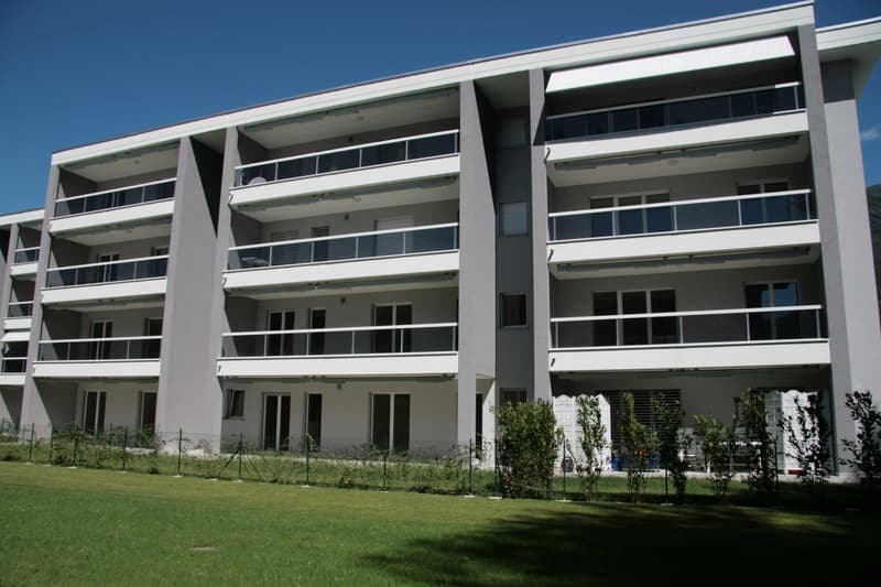Modern apartment building, multiple floors, balconies, glass windows, green lawn in front