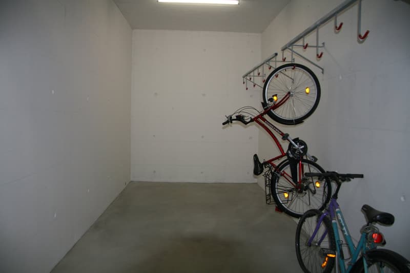 Empty room with white walls, concrete floor, ceiling light, bicycle hooks on the wall, 3 bicycles