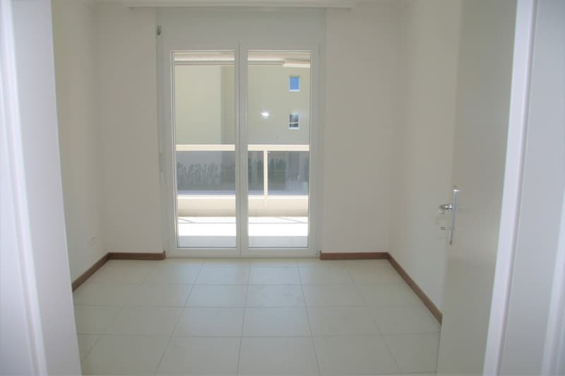 Empty room with sliding glass doors leading to a balcony, white tiled floor, white walls, power outlet on the wall