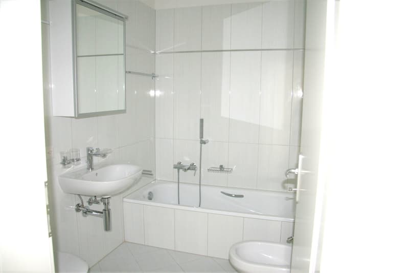 Bathroom with white tiles, bathtub, sink, mirror, and toilet.