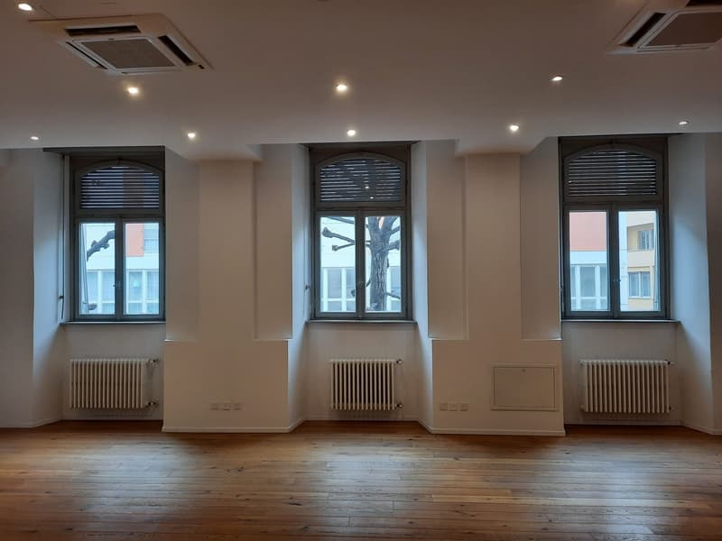 Empty room with wooden floors, white walls, radiators, and three large windows