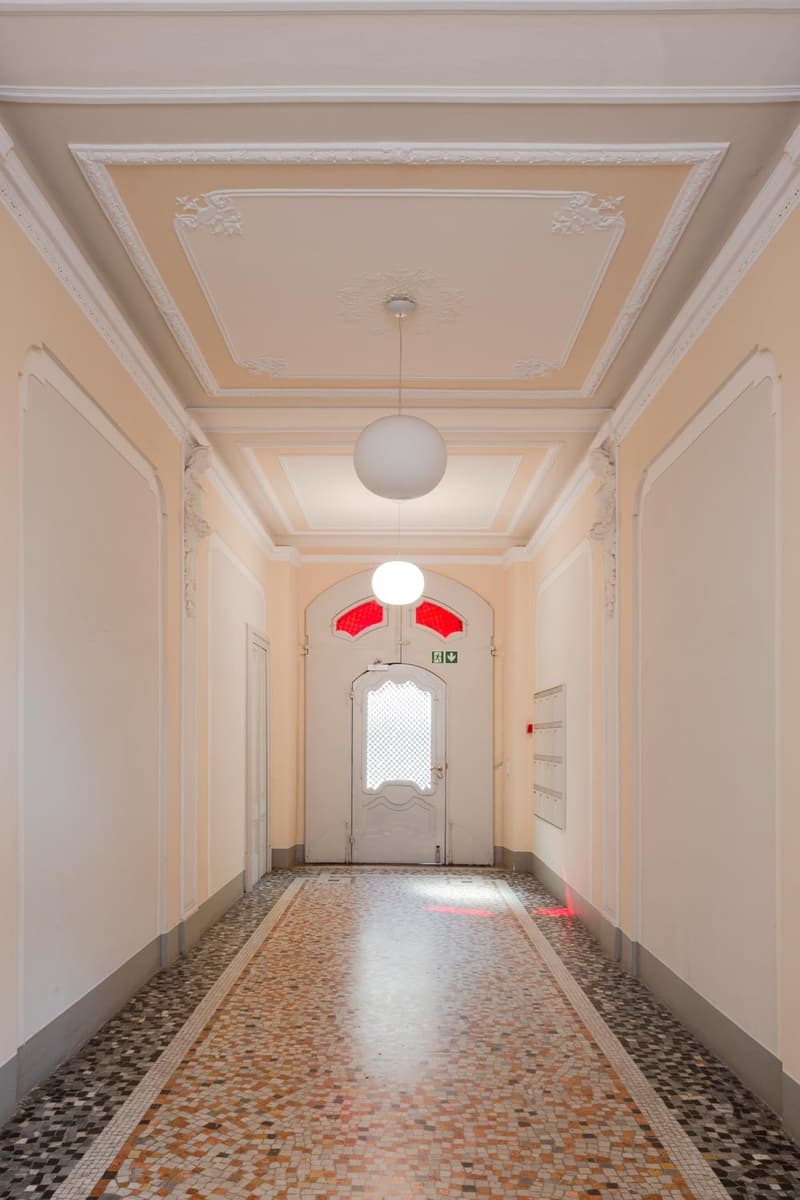 White walls, mosaic tiled floor, two hanging round lights, white doors with stained glass windows.