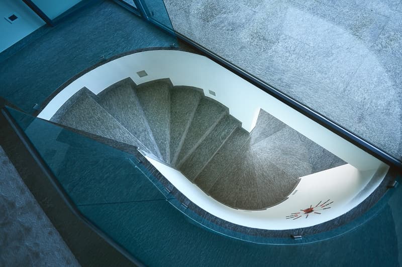 Spiral stairs with glass railing, grey carpeted steps, blue floor tile, white walls, decorative red clock