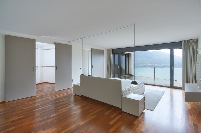 Minimalist design, large double bed, white furniture, hardwood floor, modern lamps, floor to ceiling windows with a stunning lake view, sliding doors.