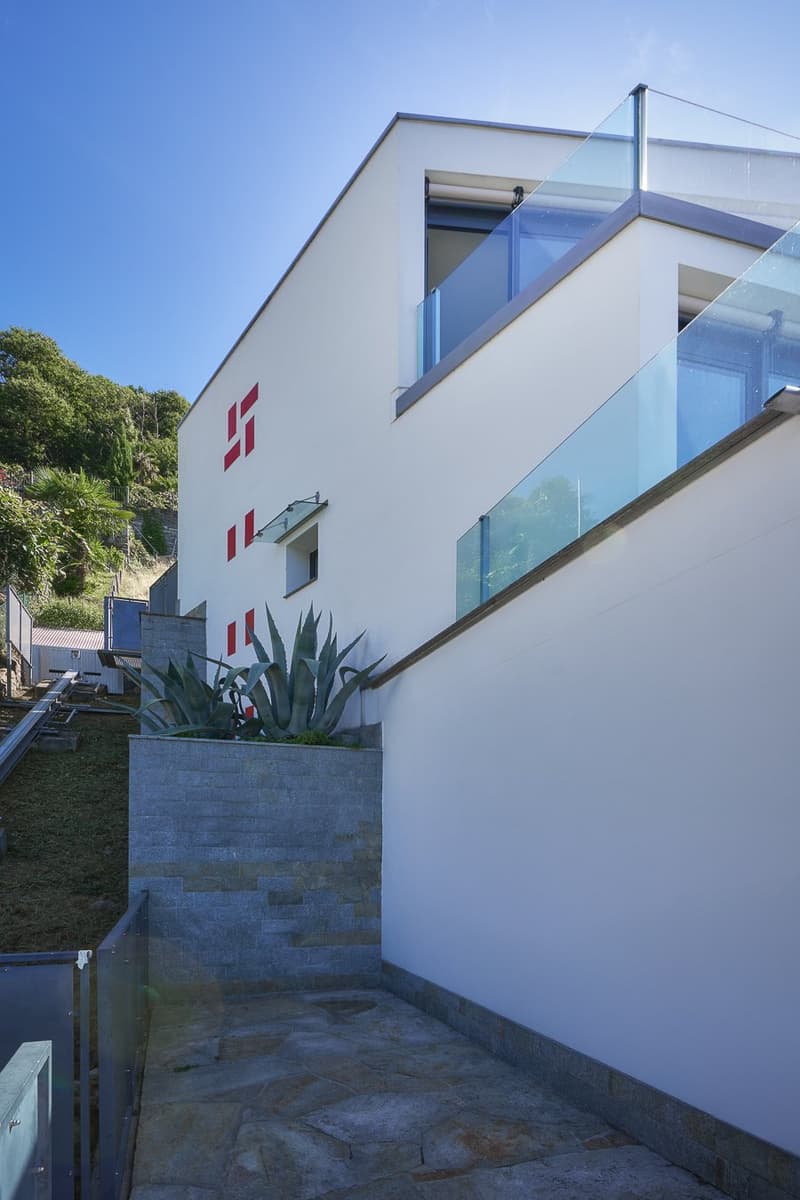 modern white building, large glass balcony, stone retaining wall with a plant, paved pathway