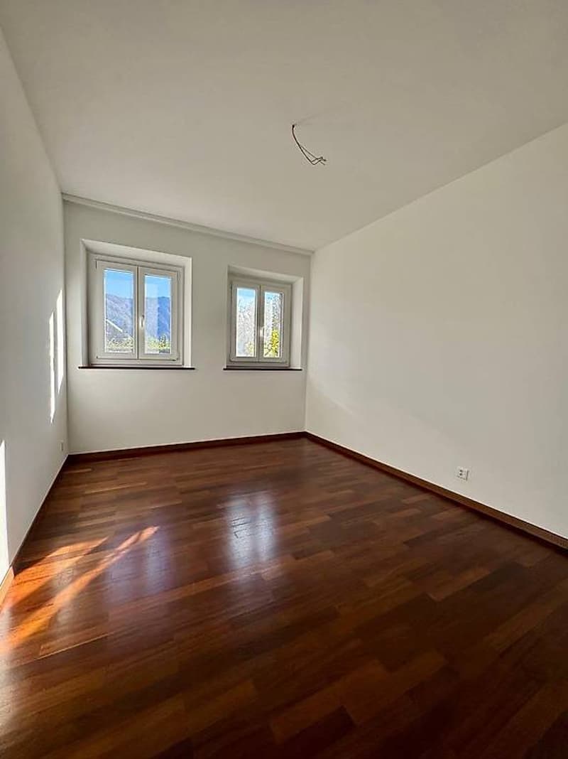 empty room with wooden floor, two windows, white walls