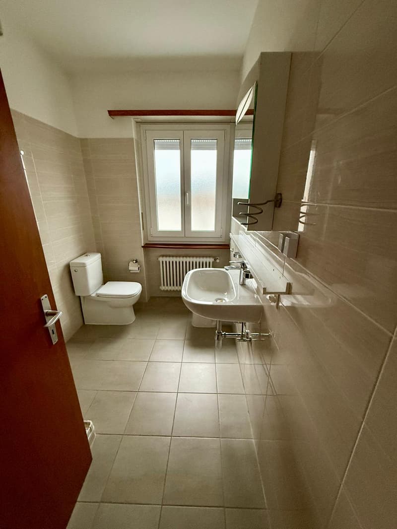 Bathroom with toilet, sink, and window with radiator.