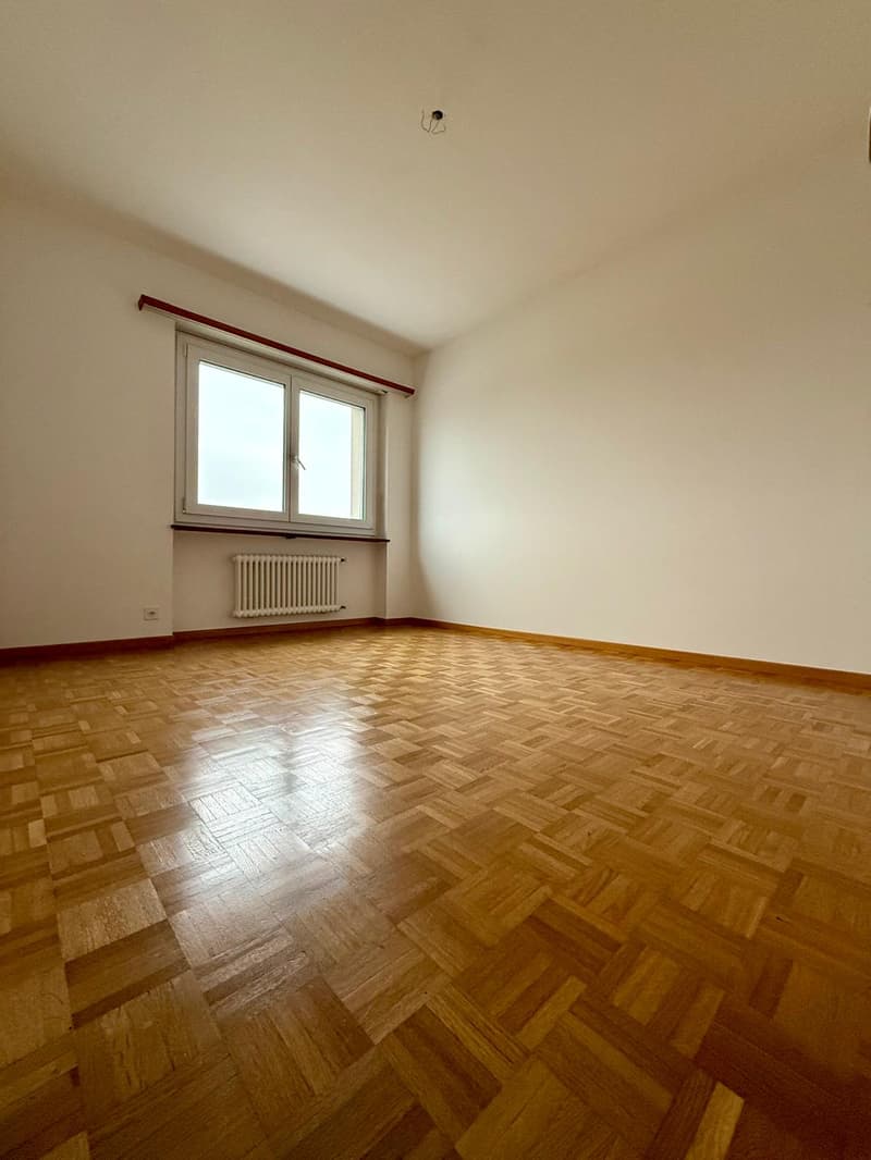 Empty room, wooden parquet flooring, white walls, glass window, radiator, electrical outlet