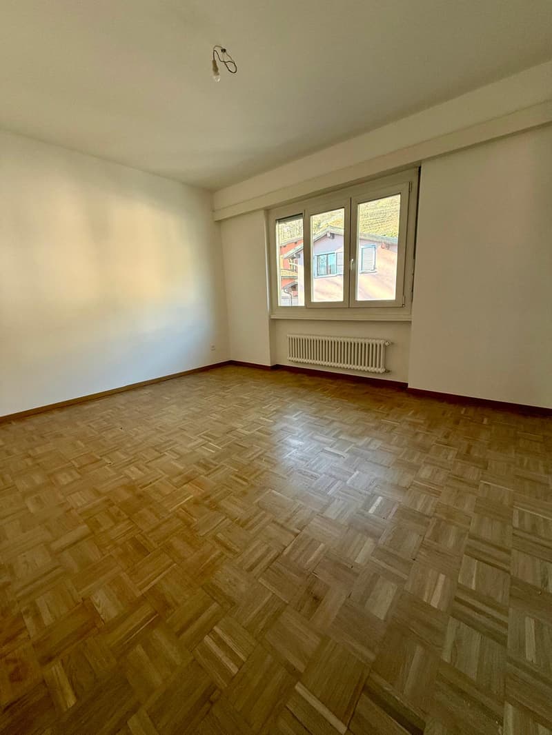 large room with wooden floor, white walls, two windows, radiator