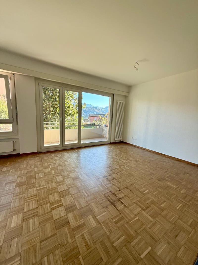 wooden floors, large windows, sliding glass doors to balcony, white walls, two windows on one wall, balcony with metal railing