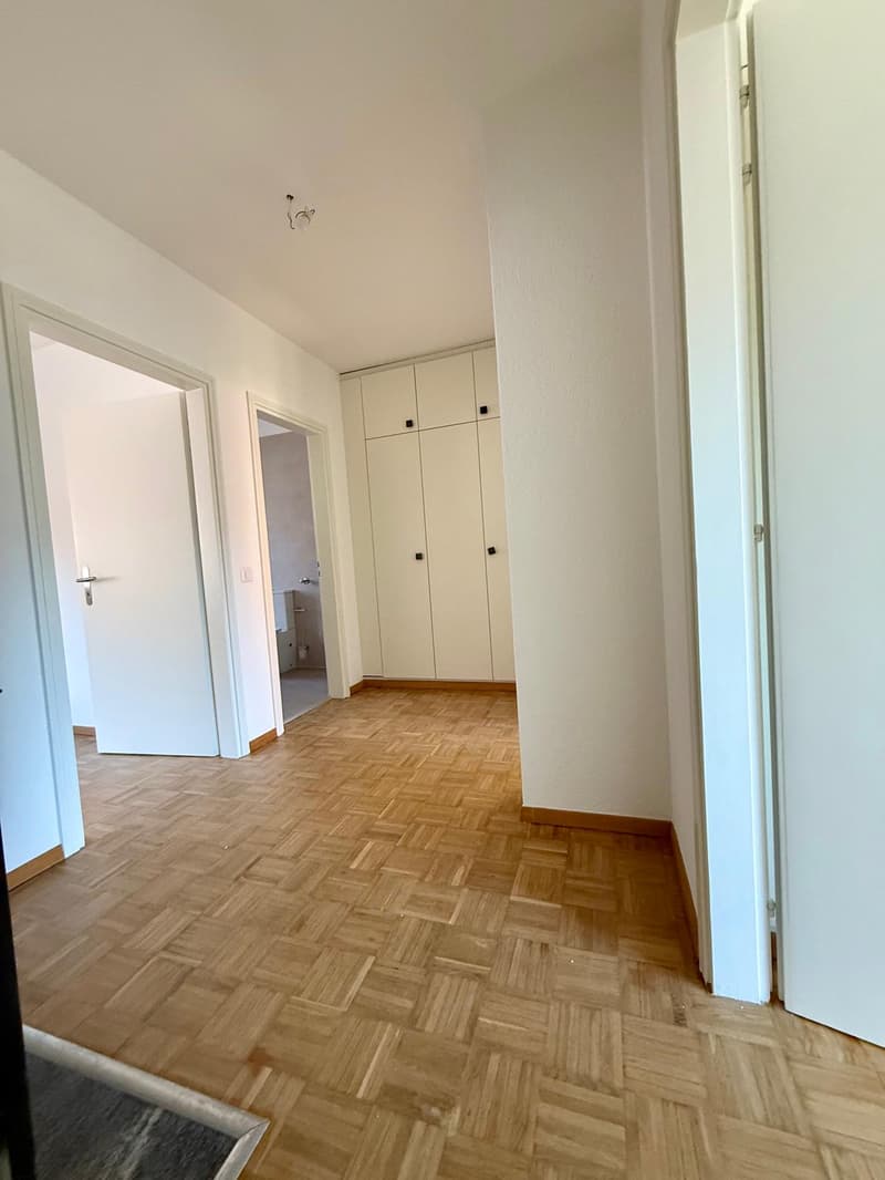 Empty room, wooden parquet floor, white walls, three open doors, one closed door, white cabinets, closed bathroom door