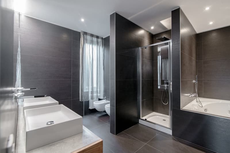 Modern bathroom with gray tiles, double sink, walk-in shower, bathtub, and toilet.