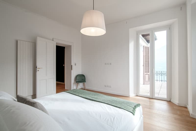 modern room, white walls, wooden floor, bed with white sheets, white and green blankets, green chair, lamps